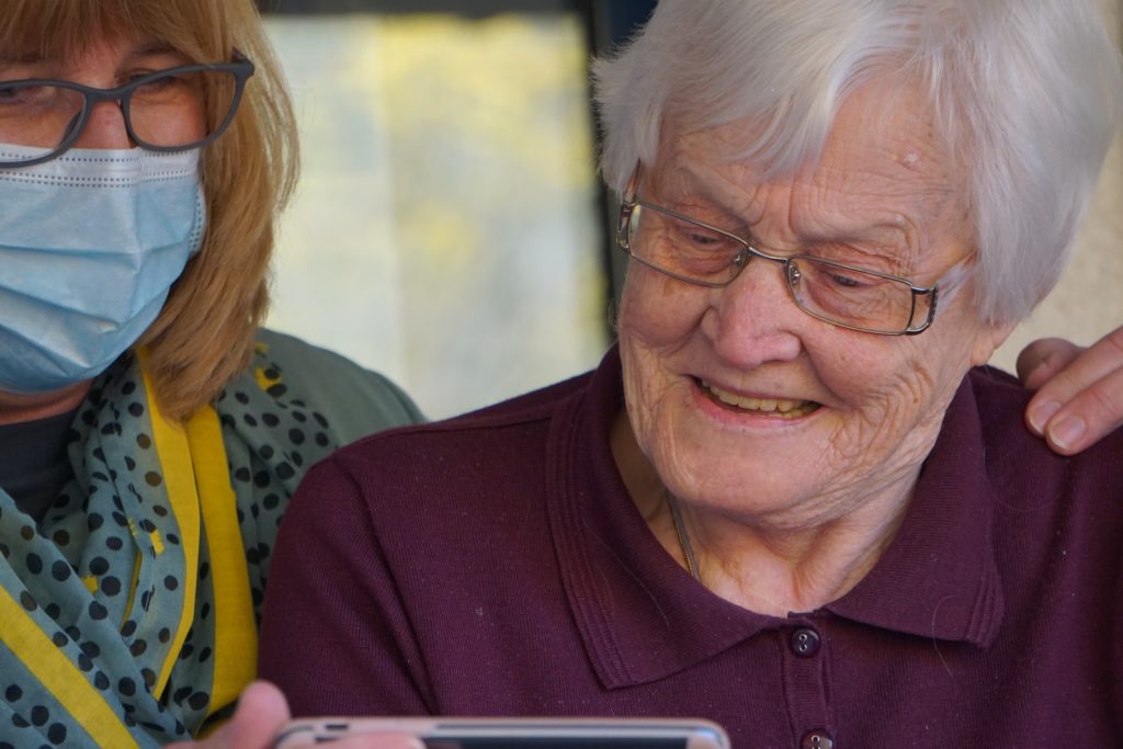 cuidadora de ancianos con señora mayor sonriendo mientras ven un móvil juntas